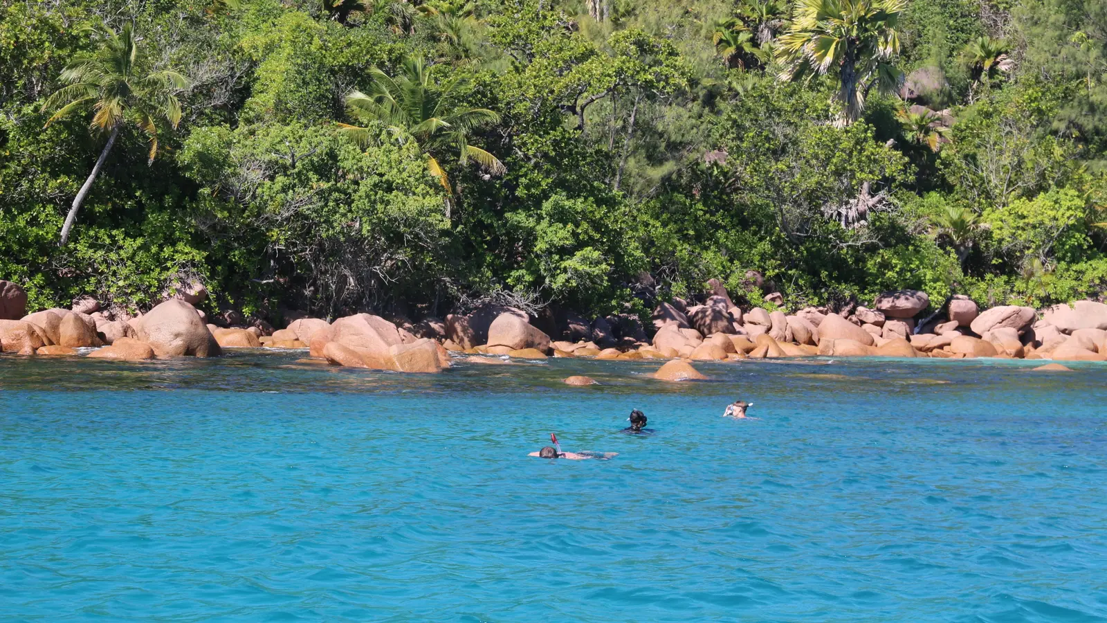 Nageurs en snorkeling dans un lagon turquoise devant des rochers de granit